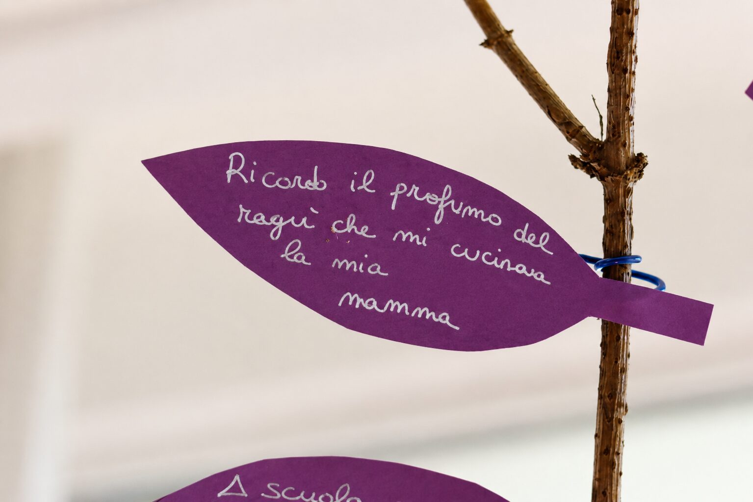 Una foglia di carta viola legata a un ramo, con scritto a mano &laquo;Ricordo il profumo del rag&ugrave; che mi cucinava la mia mamma&raquo;