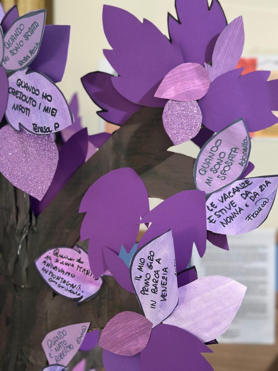 Foglie di carta viola appese a un tronco, ognuna con un ricordo scritto a mano e firmato