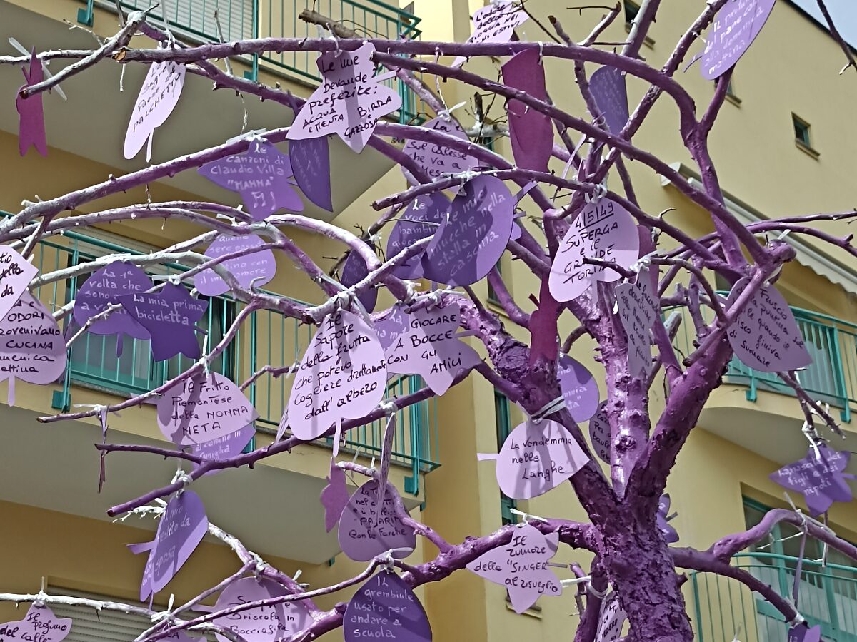 Un albero dei ricordi con il tronco dipinto di viola e le foglie scritte a mano