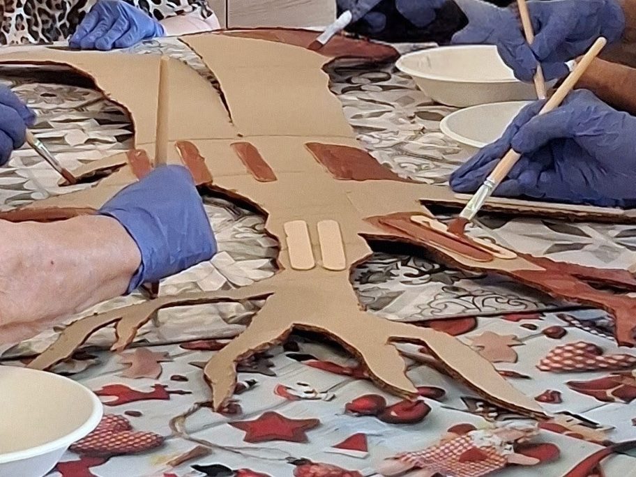 Mani con i guanti dipingono a pennello la sagoma di cartone dell'albero