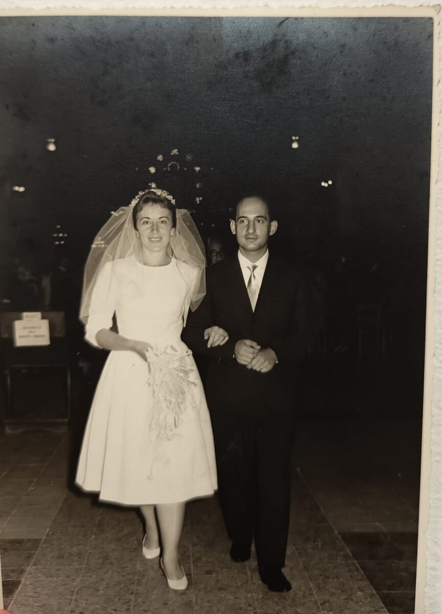 Fotografia d&rsquo;epoca in bianco e nero virata seppia: due sposi escono dalla chiesa a braccetto, lei con velo e bouquet