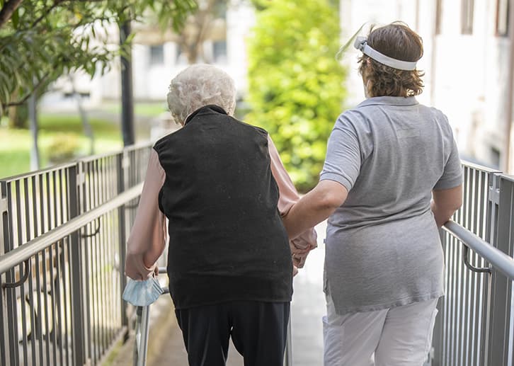 foto operatrice RSA che passeggia con anziana ospite