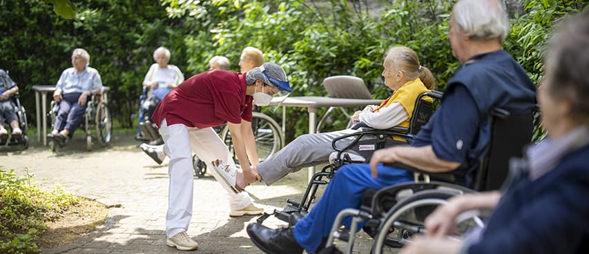 foto operatrice RSA che fa fare esercizio a ospite con patologie ortopediche in giardino